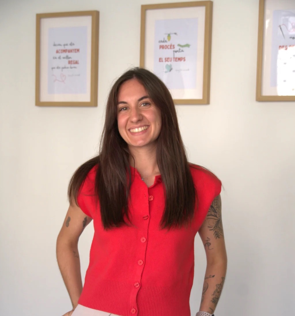 Xènia Torrent, fundadora de Fil Vermell, somrient, amb jersei vermell davant de làmines emmarcades
